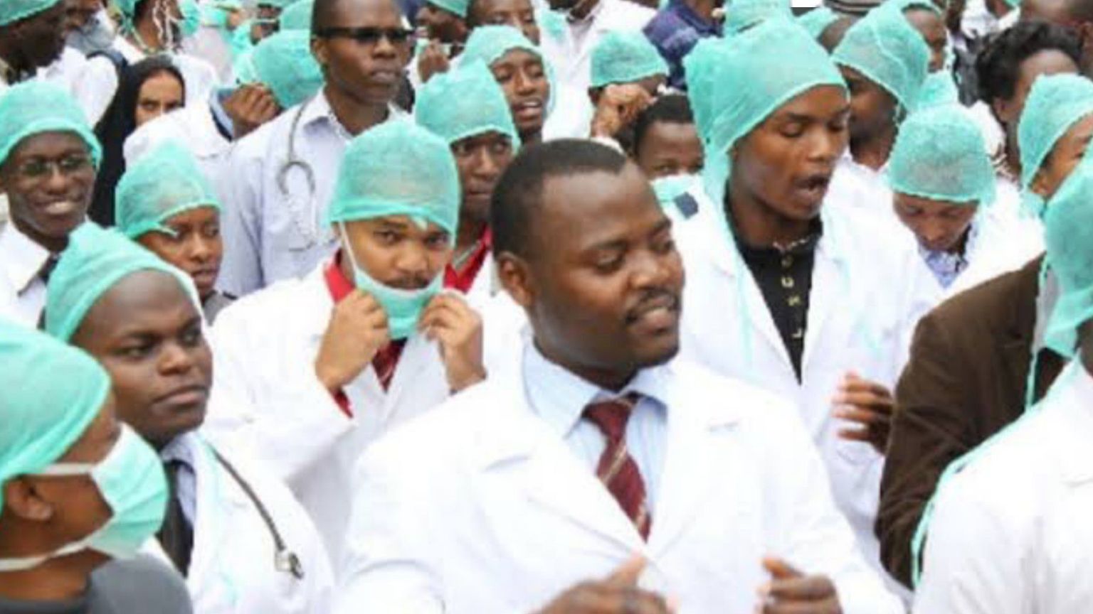 Nigerian doctors in white coats and surgical caps gathered together in protest or rally inside a hospital setting.