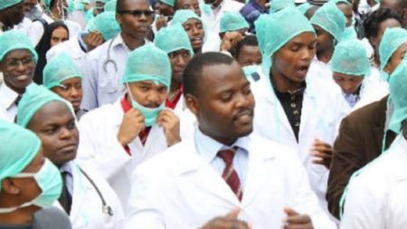 Nigerian doctors in white coats and surgical caps gathered together in protest or rally inside a hospital setting.