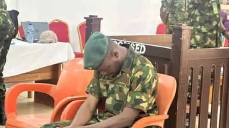 Private Lookman Musa, a Nigerian soldier, sits in a courtroom with his head bowed while wearing military camouflage uniform and a green beret, during trial proceedings over the killing of a tricycle rider.