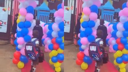 Young schoolchildren with backpacks walk through a balloon-decorated entrance on a red carpet as part of a colourful welcome ceremony at school.
