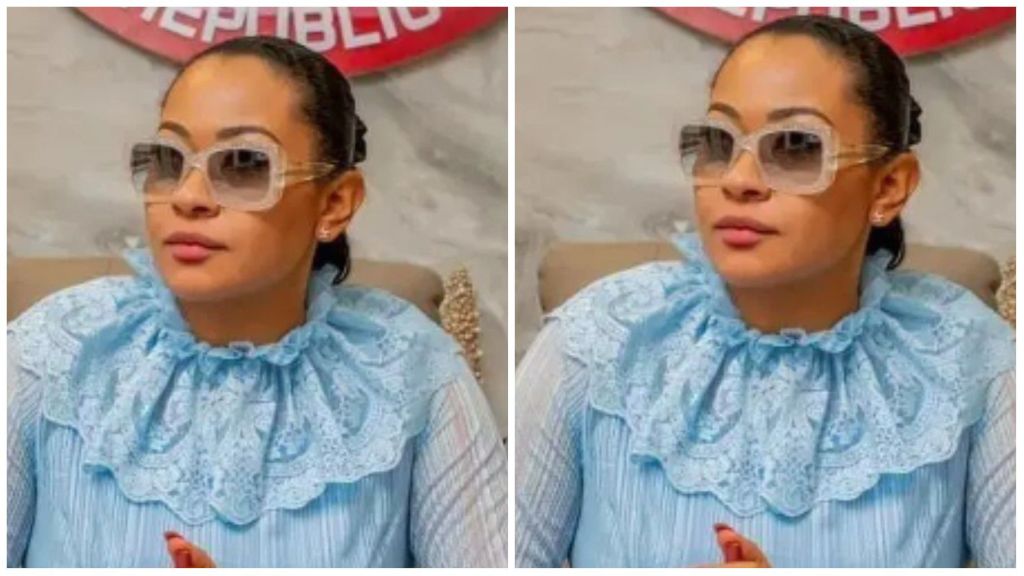 Senator Natasha Akpoti-Uduaghan sits in a light blue lace-detailed blouse, wearing large sunglasses and looking slightly to the side.
