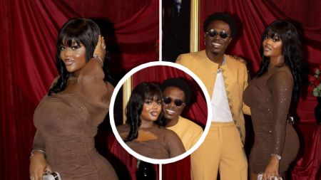 Singer Spyro poses with his fiancée at an event, with Spyro dressed in a mustard yellow outfit and his fiancée in a fitted brown gown, striking confident poses against a red curtain backdrop.