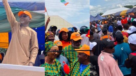 Crowd gathers at a political rally in Nigeria with supporters wearing orange ADC-branded caps and green outfits, as a party leader waves from the stage while people cheer and wave flags.
