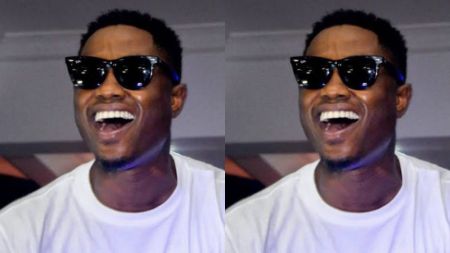 Nigerian rapper Vector captured in a mirrored photo effect, smiling widely in dark sunglasses and a white T-shirt during an event.