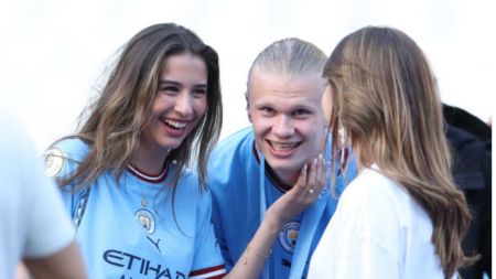 Erling Haaland and his girlfriend share a laugh while chatting with a friend during a Manchester City event. Both are seen wearing the club’s blue jerseys.