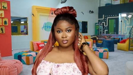 BBNaija Season 10 housemate Imisi poses inside the Big Brother Naija house lounge, wearing a floral top and styled with long reddish hair tied in an updo.