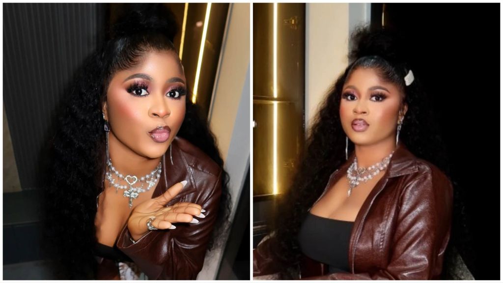 BBNaija Season 10 winner Imisi poses in a brown leather jacket and black outfit, styled with a silver heart necklace and long wavy hair, wearing soft glam makeup.