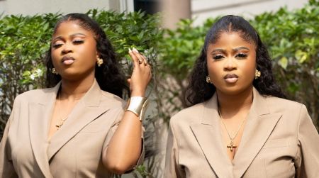 BBNaija winner Imisi poses outdoors in a beige suit, wearing gold accessories and styled hair, striking a confident look in natural light.