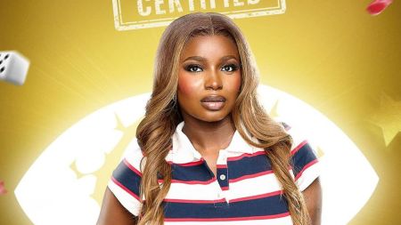 BBNaija housemate Isabella poses in her official portrait, wearing a striped polo shirt with long wavy hair styled neatly against a golden background.