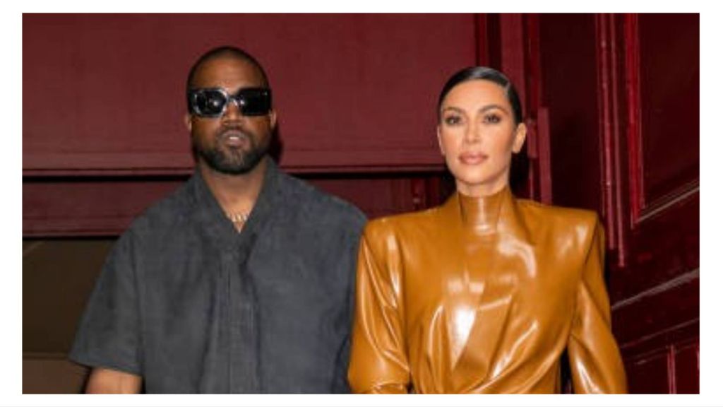 Kim Kardashian and Kanye West pose together at an event, with Kardashian in a brown leather outfit and West in a dark shirt.