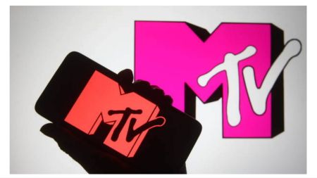 A hand holding a smartphone with the red MTV logo displayed on the screen, positioned in front of a large pink MTV logo projected on a wall.