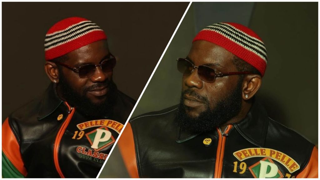 Nigerian rapper Odumodublvck wearing dark sunglasses, a red-striped cap, and a black Pelle Pelle leather jacket, posing confidently indoors.