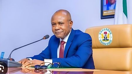 Enugu State Governor Peter Mbah seated at his desk in a blue suit, speaking into a microphone during an official address at Government House, Enugu.