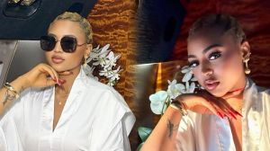 Regina Daniels poses elegantly in a luxury setting wearing a white silk robe, gold accessories, and sunglasses, with white orchids in the background.