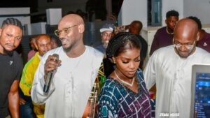 2Baba (Innocent Idibia) speaks into a microphone while smiling at a small birthday gathering, with his wife Hon. Natasha Osawaru Idibia standing beside him in a patterned outfit. Friends and guests are seen in the background, capturing the relaxed celebration atmosphere.