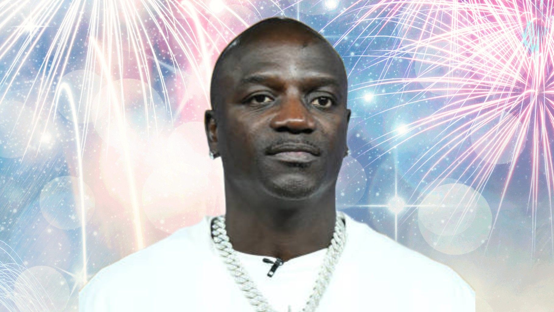 Akon stands against a bright, colourful background filled with fireworks and glowing light effects while wearing a white shirt and a silver chain.