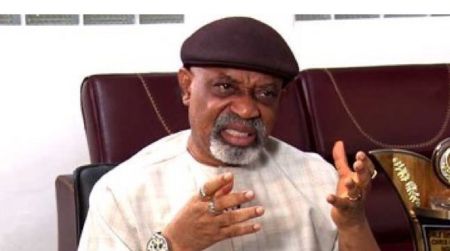 Chris Ngige speaking during an interview, gesturing with both hands while seated on a brown leather chair.