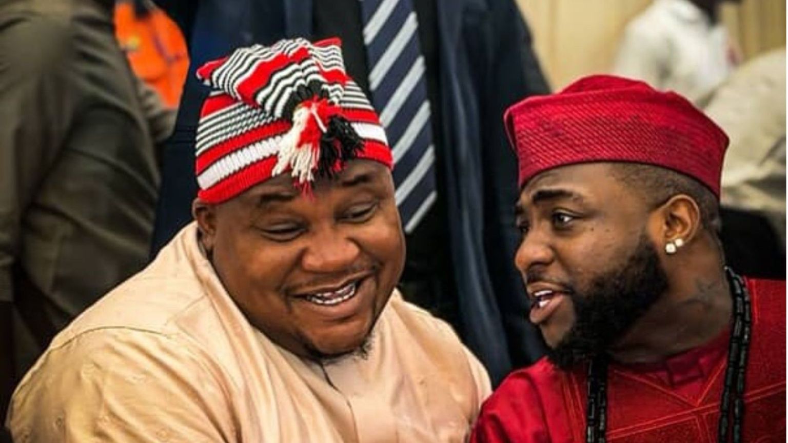Cubana Chief Priest and Davido sitting close together, smiling and talking while dressed in traditional outfits at an event.