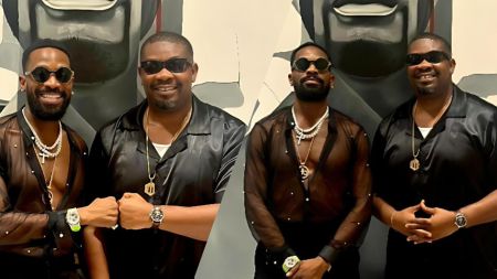 Dbanj and Don Jazzy stand together smiling in stylish black outfits, wearing sunglasses and jewelry, posing in front of a monochrome artwork.