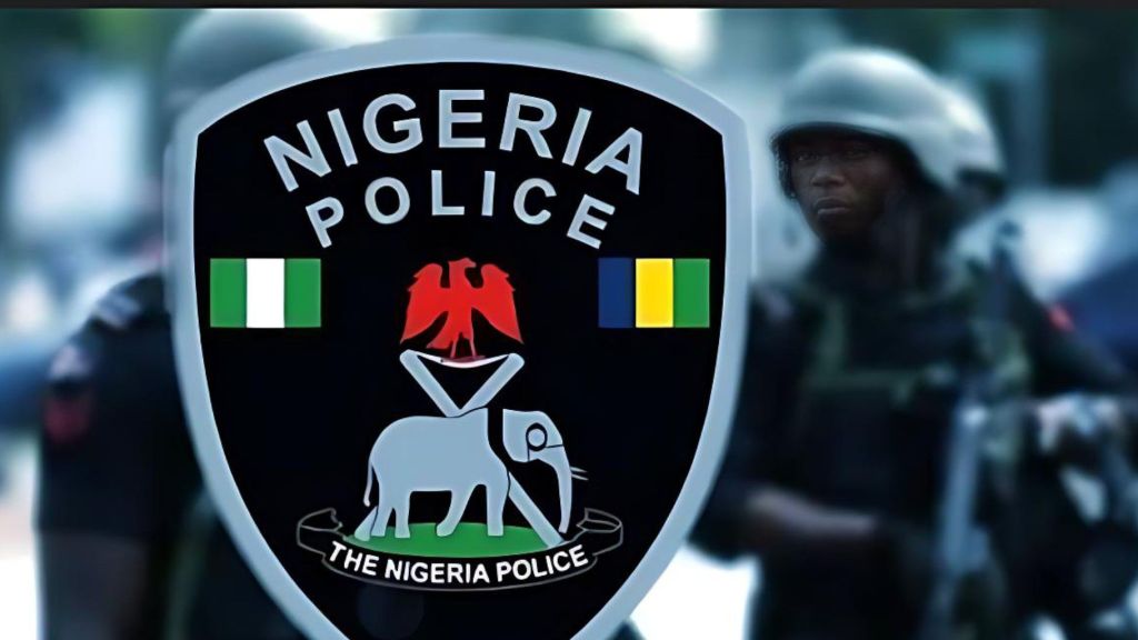 A close-up of the Nigeria Police Force emblem, featuring an eagle, crossed staves, and an elephant, with armed police officers blurred in the background.