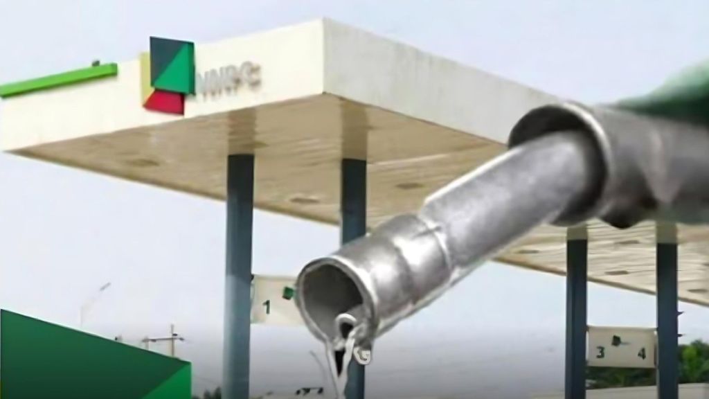 Close-up of a fuel nozzle dripping petrol in front of an NNPC filling station canopy.