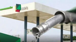 Close-up of a fuel nozzle dripping petrol in front of an NNPC filling station canopy.