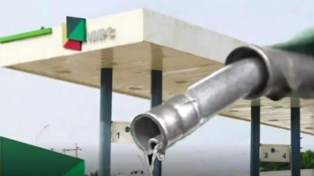 Close-up of a fuel nozzle dripping petrol in front of an NNPC filling station canopy.