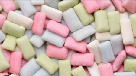 A close-up image showing many pieces of pastel-coloured chewing gum, including pink, white, green and light grey pieces, scattered together.