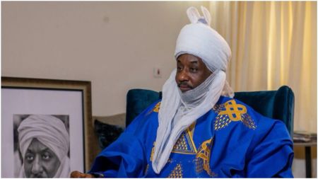 A portrait of Emir Sanusi, a Nigerian traditional ruler, seated and wearing a royal blue robe with gold embroidery and a white turban.