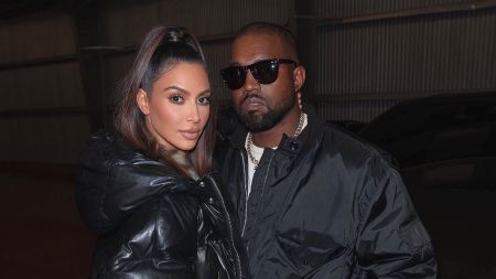 Kim Kardashian and Kanye West stand closely together in dark outerwear, posing indoors with a calm, serious look.