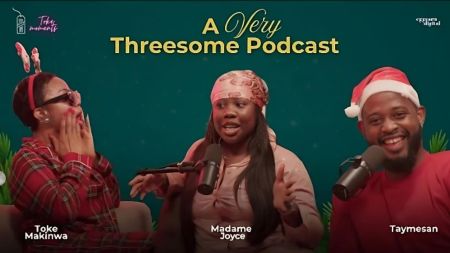 Promotional graphic for "A Very Threesome Podcast" episode on Toke Moments YouTube channel, featuring a festive Christmas-themed setup with a teal starry background—left: Toke Makinwa in a red plaid outfit and headband, hands covering mouth in surprise; center: Madame Joyce in a beige hoodie and patterned headscarf, speaking into a microphone; right: Taymesan in a red shirt and Santa hat, smiling while holding a microphone.