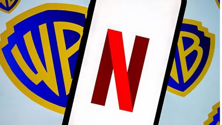 A smartphone screen showing the red Netflix “N” logo placed in front of multiple blue and gold Warner Bros shield logos.