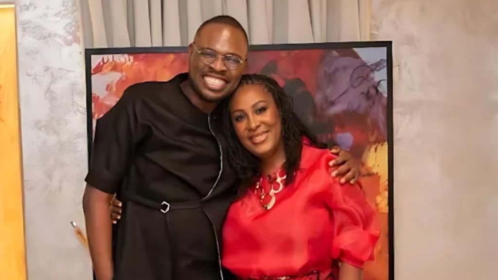 Chude Jideonwo and Uju Anya pose together for a photo. Chude wears a black outfit and glasses, smiling widely with his arm around Uju, who is wearing a bright red blouse and smiling.