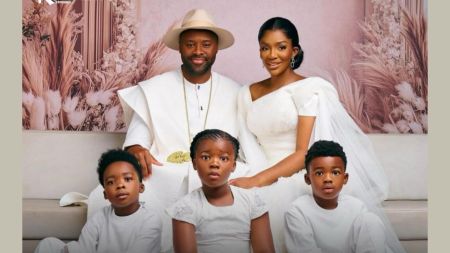 The Olu of Warri, Ogiame Atuwatse III, seated with his wife Queen Ivie Atuwatse and their three children, two boys and a girl, all dressed in matching white traditional outfits for a family portrait.