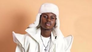 Nigerian streamer and TikTok star Peller posing in a stylish white outfit and white fur hat against a beige studio background.
