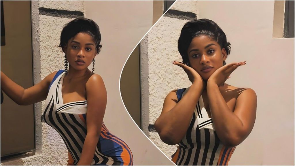 A split collage features two photos of BBNaija star Phyna posing in a fitted, sleeveless dress with black, white, blue, and orange vertical stripes. On the left, she stands against a white wall, looking seriously at the camera with one hand resting on a doorframe. On the right, in a circular insert, she frames her face with both hands, maintaining a calm, direct gaze. She wears dangling earrings and sports a short, sleek black hairstyle in both shots.