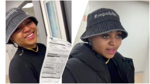 Regina Daniels smiles while holding a medical document and wearing a black outfit with a denim bucket hat labeled Republic, appearing to speak to someone off-camera in a hallway.