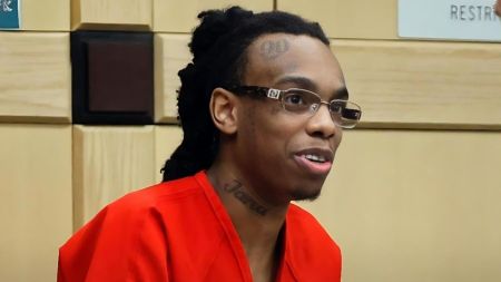 YNW Melly wins legal victory as witness tampering charges drop YNW Melly (Jamell Demons) appearing in court wearing an orange prison jumpsuit and glasses. He is smiling and looking to the side, with visible tattoos on his forehead ("90") and neck ("Jana").