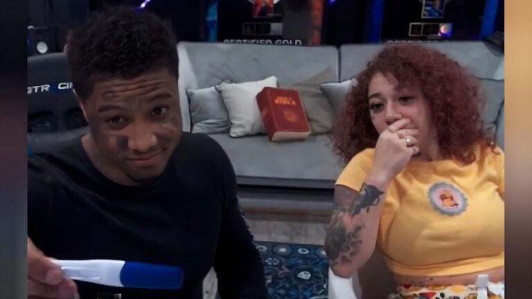 A screenshot from a livestream featuring rapper Blueface and his girlfriend Nevaeh Akira. Blueface, on the left, is wearing a black long-sleeved shirt and holds a positive blue pregnancy test toward the camera with a slight smile. To the right, Nevaeh, with curly reddish-brown hair and a yellow t-shirt, looks surprised with her hand over her mouth. In the background, a gray sofa holds a white pillow and a large red book labeled "HOLY BIBLE."